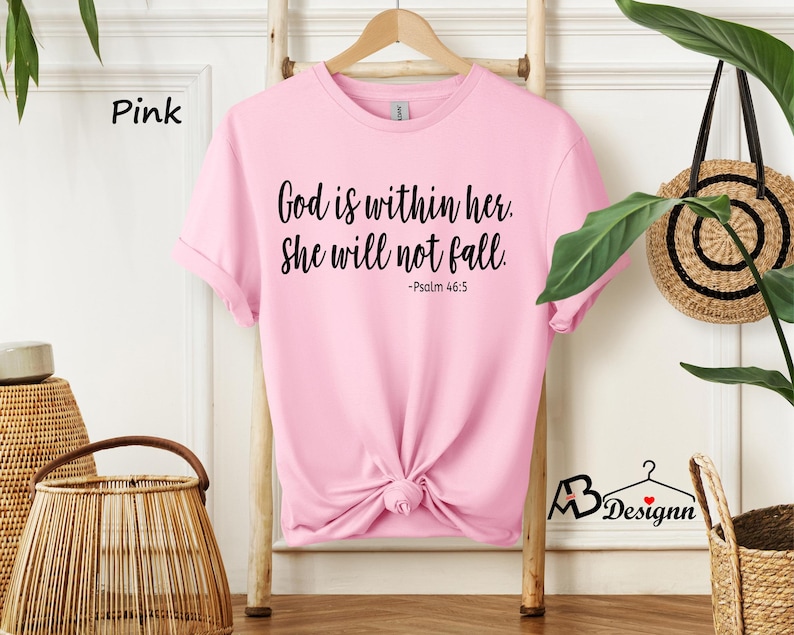 Peut inclure: T-shirt rose avec le texte "God is within her. She will not fall. -Psalm 46:5" imprim&eacute; en noir.