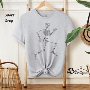 May include: A grey t-shirt with a skeleton running on the front. The skeleton is labeled with the names of the bones. The shirt is on a hanger and has the words "Sport Grey" written on a tag.
