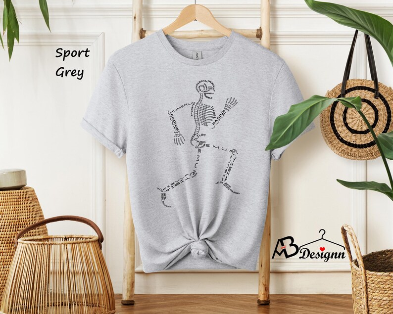 May include: A grey t-shirt with a skeleton running on the front. The skeleton is labeled with the names of the bones. The shirt is on a hanger and has the words "Sport Grey" written on a tag.