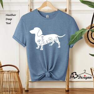 May include: A heather deep teal t-shirt featuring a white outline of a dachshund with floral details. The shirt is on a wooden hanger.