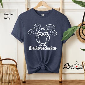May include: A navy blue t-shirt with a white graphic of a cartoon chicken wearing glasses and surrounded by math equations. The text "Mathemachicken" is printed below the chicken.