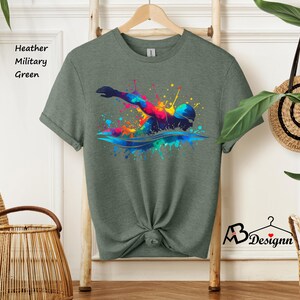 May include: A heather military green t-shirt with a colorful graphic of a swimmer in a splash of paint.