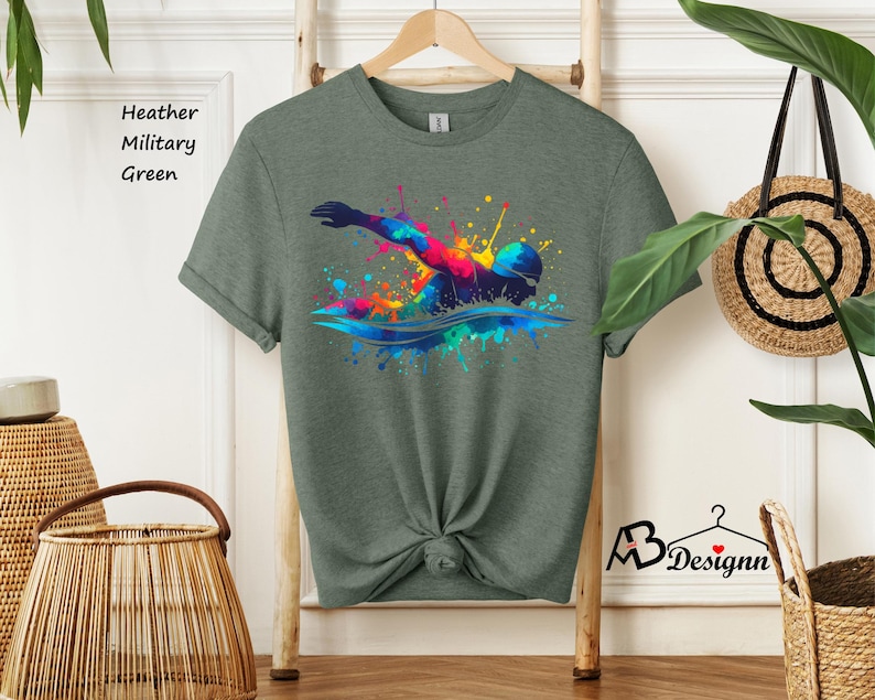 May include: A heather military green t-shirt with a colorful graphic of a swimmer in a splash of paint.