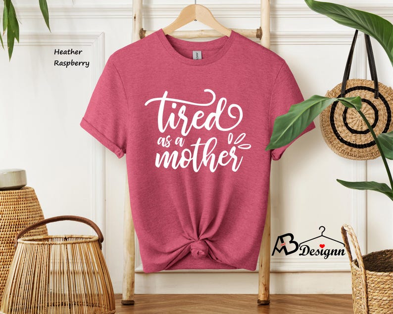 May include: A heather raspberry t-shirt with the text "Tired as a mother" in white lettering.