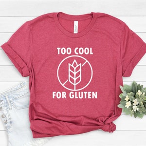 May include: A red t-shirt with white text that reads "Too Cool For Gluten" and a white graphic of a crossed-out wheat stalk.