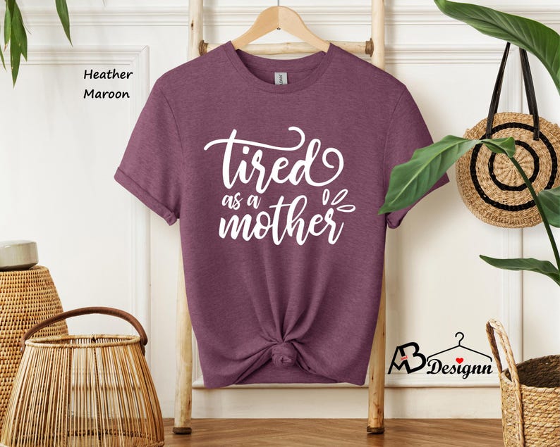 May include: A heather maroon t-shirt with the text "tired as a mother" in white.
