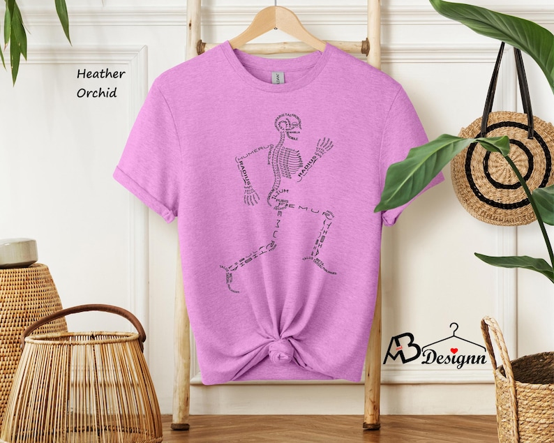 May include: A heather orchid t-shirt with a skeleton graphic. The skeleton is running and the bones are labeled with their anatomical names.