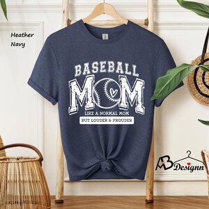 May include: A heather navy blue t-shirt with the text "Baseball Mom" in white. The text is surrounded by a baseball graphic and the text "Like a normal mom but louder & prouder".