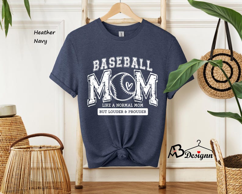 May include: A heather navy blue t-shirt with the text "Baseball Mom" in white. The text is surrounded by a baseball graphic and the text "Like a normal mom but louder & prouder".
