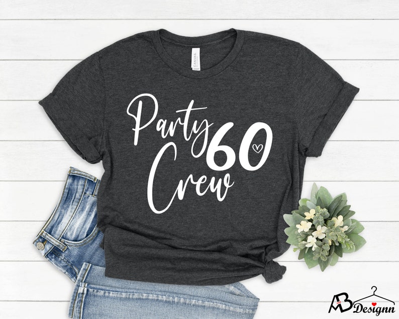May include: A dark gray t-shirt with white text that reads "Party 60 Crew" with a small heart symbol next to the number 60.