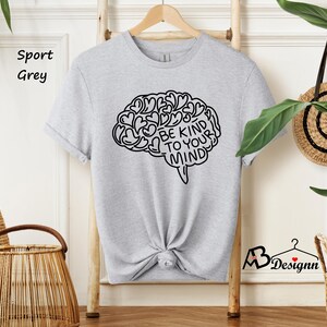 May include: A gray sport t-shirt with a black outline of a brain with hearts inside and the text "Be Kind To Your Mind".