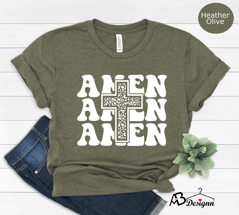May include: A green t-shirt with a white graphic of the word "Amen" repeated three times with a cross in the center. The cross is filled with a floral pattern.