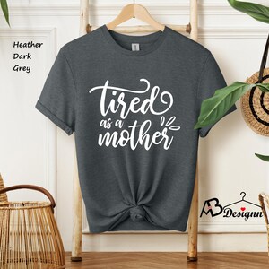 May include: A dark heather grey t-shirt with the text "tired as a mother" in white lettering.