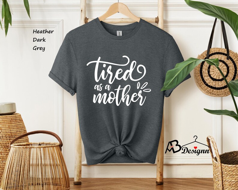 May include: A dark heather grey t-shirt with the text "tired as a mother" in white lettering.