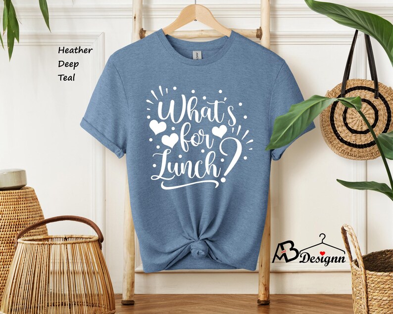 K&ouml;nnte beinhalten: Ein T-Shirt in der Farbe Heide-Tiefe Teal mit dem Text "What's for Lunch?" in Wei&szlig;. Der Text ist von drei wei&szlig;en Herzen umgeben.