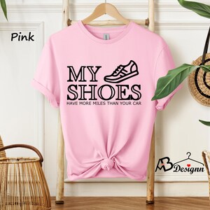 May include: Pink t-shirt with a black graphic that says "My Shoes Have More Miles Than Your Car" and a black illustration of a sneaker.