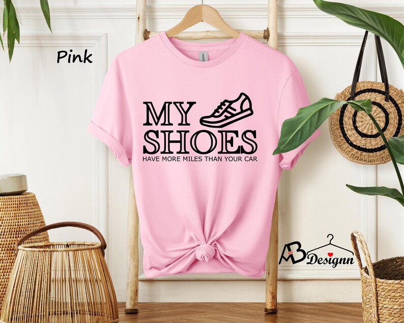 May include: Pink t-shirt with a black graphic that says "My Shoes Have More Miles Than Your Car" and a black illustration of a sneaker.