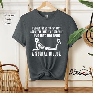 May include: Dark heather grey t-shirt with a white skeleton graphic and the text "People need to start appreciating the effort I put into not being a serial killer".