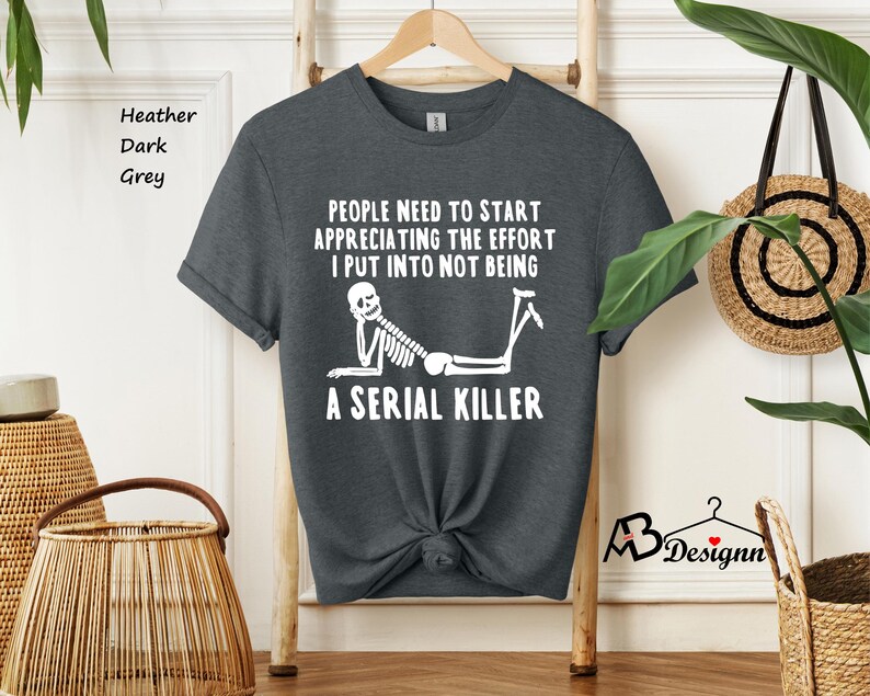May include: Dark heather grey t-shirt with a white skeleton graphic and the text "People need to start appreciating the effort I put into not being a serial killer".