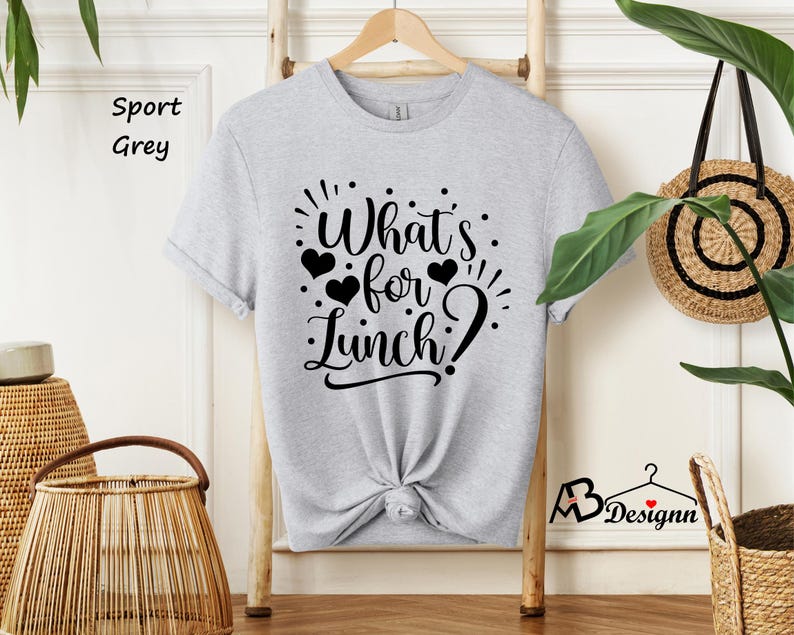 K&ouml;nnte beinhalten: Ein graues T-Shirt mit dem Text "What's for Lunch?" in schwarzer Schrift. Der Text ist von kleinen schwarzen Herzen umgeben.