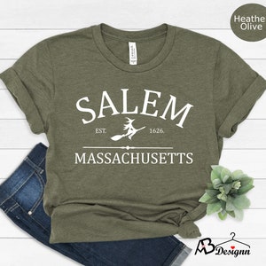 May include: A green t-shirt with white text that reads "SALEM EST. 1626. MASSACHUSETTS" with a witch flying on a broomstick in between the words "SALEM" and "EST."