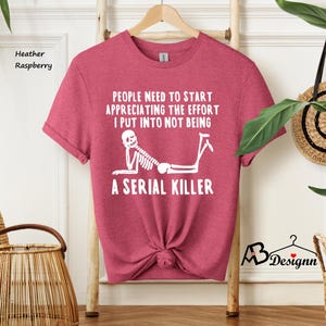 May include: A heather raspberry t-shirt with a white skeleton graphic and the text "People need to start appreciating the effort I put into not being a serial killer".