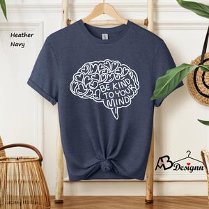 May include: A navy blue heather t-shirt with a white outline of a brain with hearts and the text "Be Kind To Your Mind".