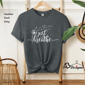 May include: A dark heather grey t-shirt with a white dandelion design and the text "just breathe".