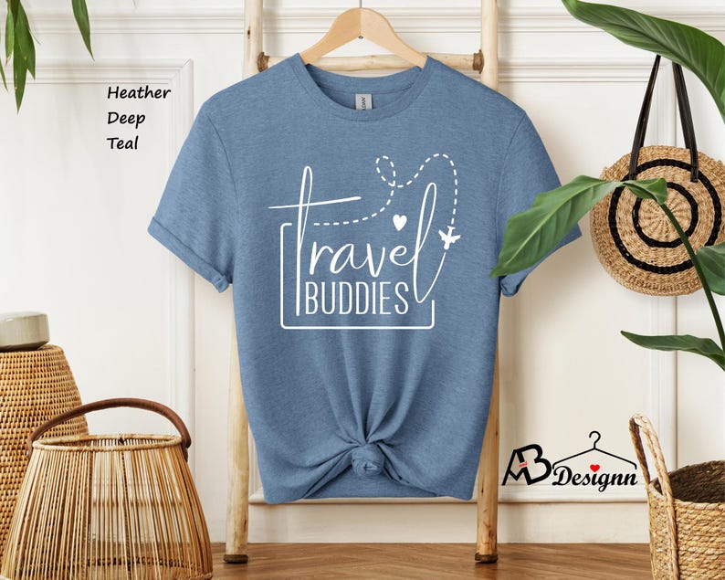 K&ouml;nnte beinhalten: Ein kurz&auml;rmeliges T-Shirt in Heather Deep Teal mit einem wei&szlig;en Grafikdruck, der travel BUDDIES liest, erg&auml;nzt durch eine gestrichelte Flugroute, ein kleines Herz und ein Flugzeugsymbol. Das T-Shirt ist in der Mitte unten zu einem Knoten gebunden.