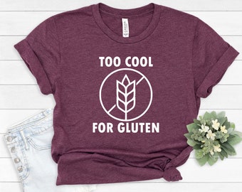 May include: A maroon t-shirt with white text that reads "Too Cool For Gluten" and a white graphic of a wheat stalk with a diagonal line through it.