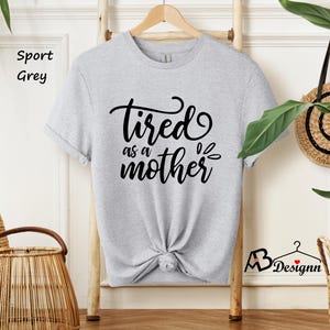 May include: A light grey t-shirt with the text "tired as a mother" in black lettering.