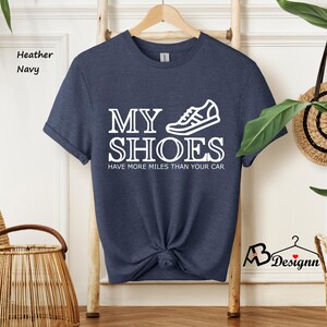 May include: A heather navy blue t-shirt with a white graphic of a running shoe and the text "My Shoes Have More Miles Than Your Car."