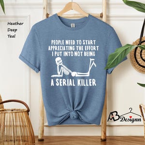 May include: A light blue t-shirt with a white skeleton graphic and the text "People need to start appreciating the effort I put into not being a serial killer".