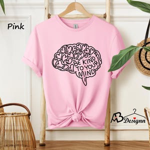 May include: Pink t-shirt with a black graphic of a brain with hearts and the text "Be Kind To Your Mind".