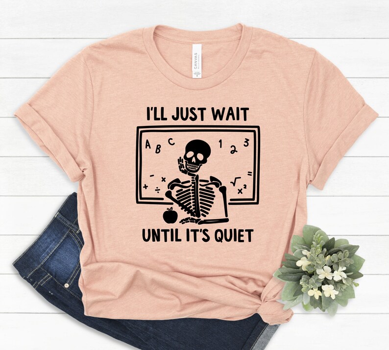 Może przedstawiać: R&oacute;żowy t-shirt z czarną ilustracją szkieletu. Szkielet siedzi przy tablicy z napisem "Po prostu poczekam, aż będzie cicho".