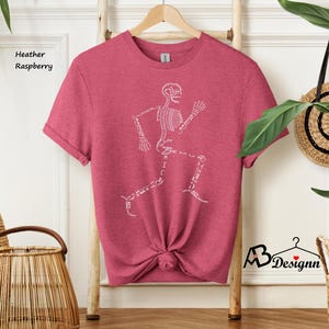 May include: Heather raspberry t-shirt featuring a white skeleton running with the names of the bones labeled. The shirt is on a wooden hanger.