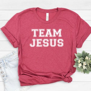 May include: A red t-shirt with white text that says "TEAM JESUS" in a varsity style font.
