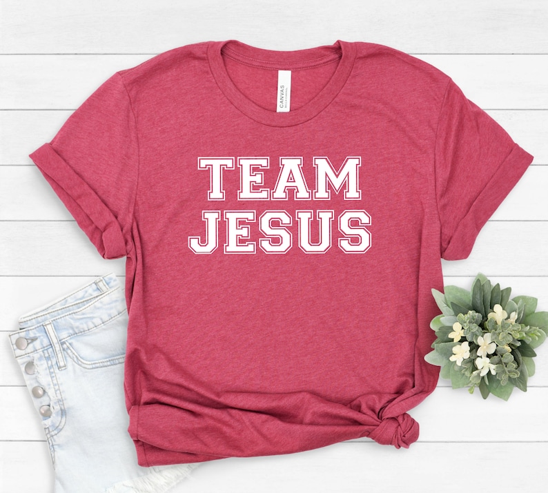 May include: A red t-shirt with white text that says "TEAM JESUS" in a varsity style font.