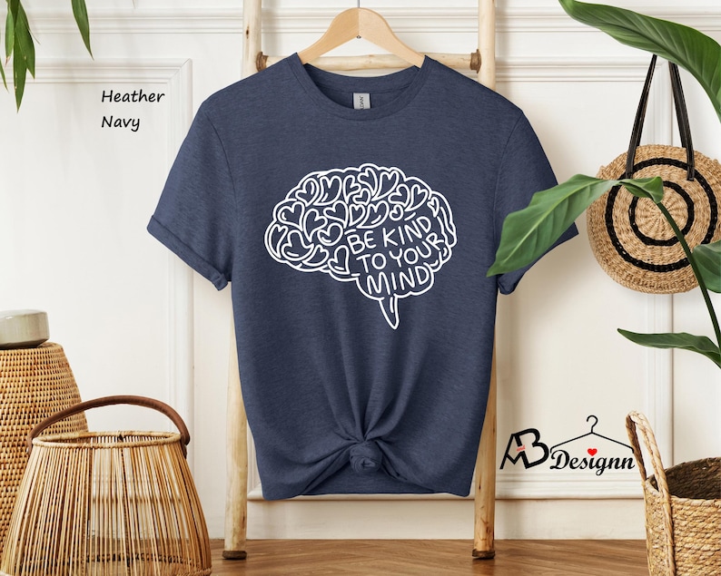 May include: A navy blue heather t-shirt with a white outline of a brain with hearts and the text "Be Kind To Your Mind".