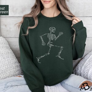 Peut inclure: Sweat-shirt vert for&ecirc;t avec un motif de coureur squelettique blanc. Les os sont &eacute;tiquet&eacute;s avec des termes anatomiques. Le sweat-shirt est de couleur unie et a un col rond.