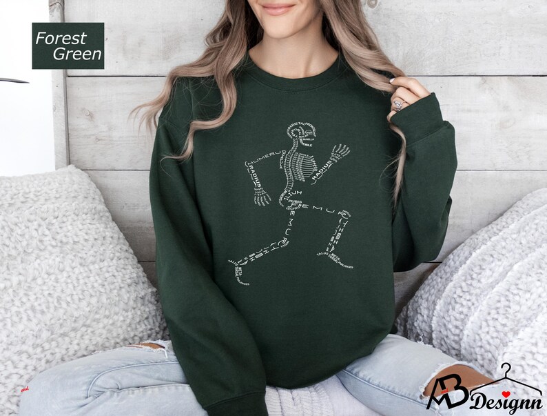 Peut inclure: Sweat-shirt vert for&ecirc;t avec un motif de coureur squelettique blanc. Les os sont &eacute;tiquet&eacute;s avec des termes anatomiques. Le sweat-shirt est de couleur unie et a un col rond.