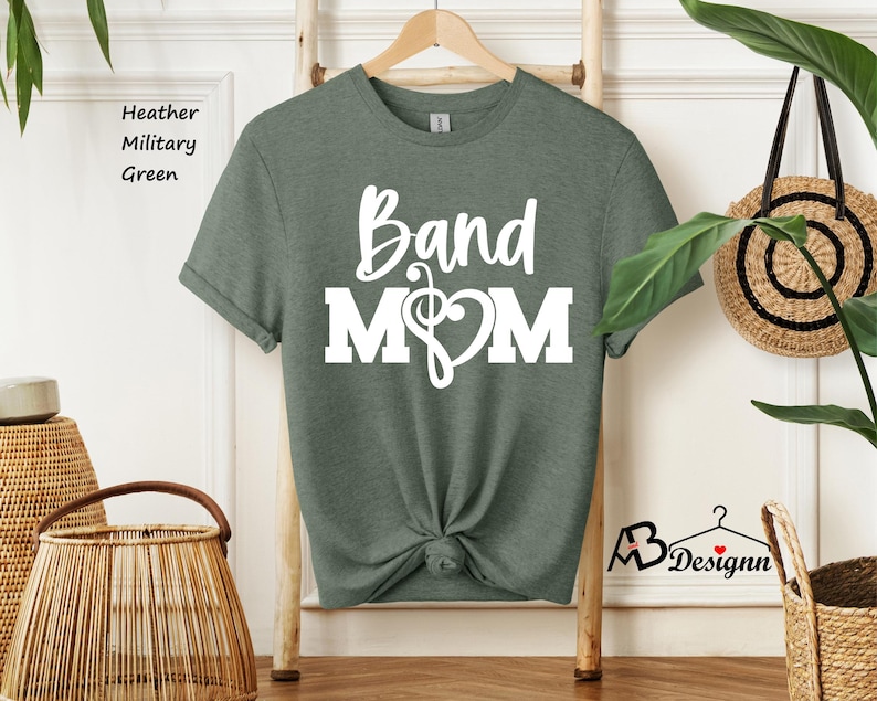 May include: A heather military green t-shirt with the text "Band Mom" in white lettering. A musical note and heart are included in the design.