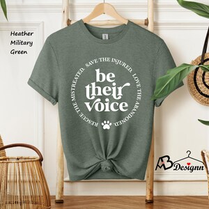 May include: Heather military green t-shirt with the text "be their voice" in a circular design. The design includes a paw print and the phrases "Rescue the mistreated, save the injured, love the abandoned."