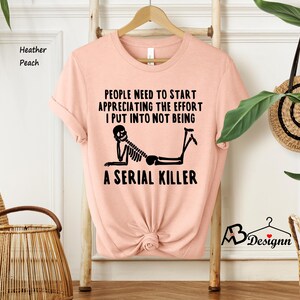 May include: A pink t-shirt with a black skeleton graphic and the text "People need to start appreciating the effort I put into not being a serial killer."