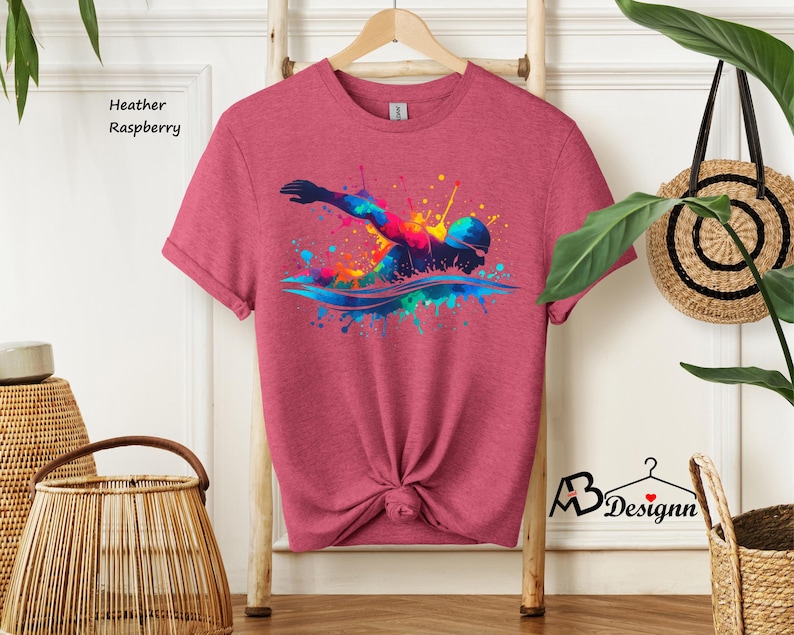 May include: Heather raspberry t-shirt with a colorful graphic of a swimmer in a splash of water.