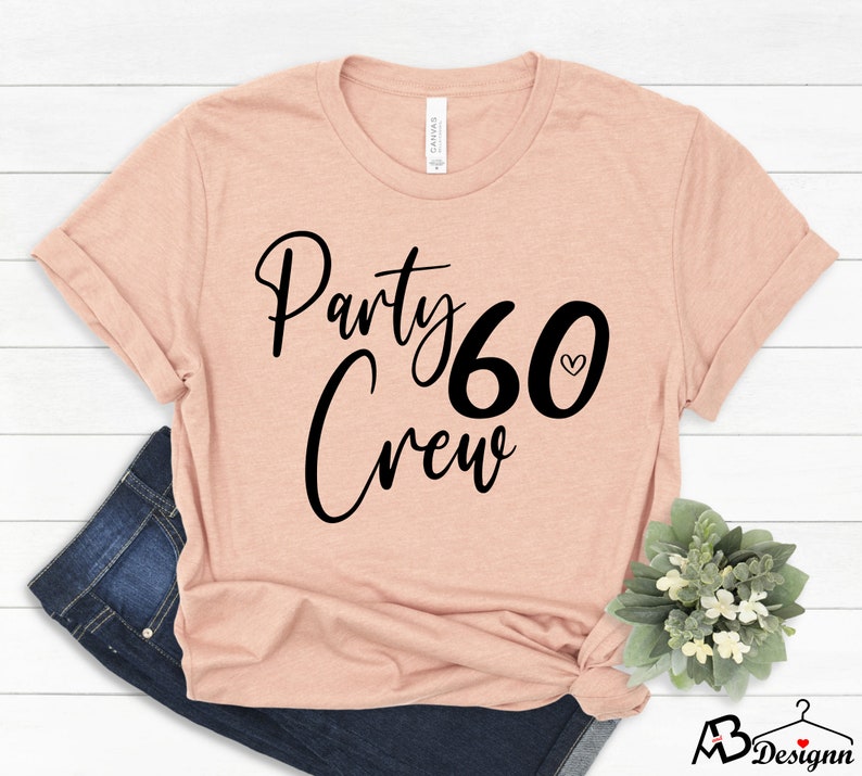 May include: A peach-colored t-shirt with the text "Party Crew 60" in black with a small heart next to the number 60.