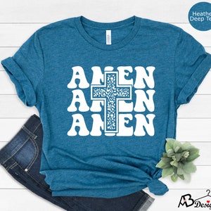 May include: A teal blue t-shirt with a white graphic of the word "Amen" repeated three times with a cross in the center. The cross is filled with a white and gray pattern.