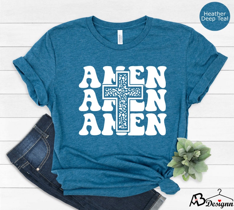 May include: A teal blue t-shirt with a white graphic of the word "Amen" repeated three times with a cross in the center. The cross is filled with a white and gray pattern.