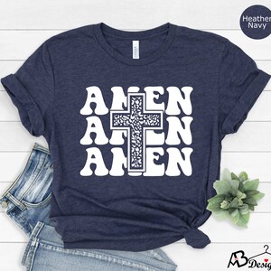 May include: A navy blue t-shirt with a white graphic of a cross and the word "AMEN" repeated three times. The cross is filled with a floral pattern.