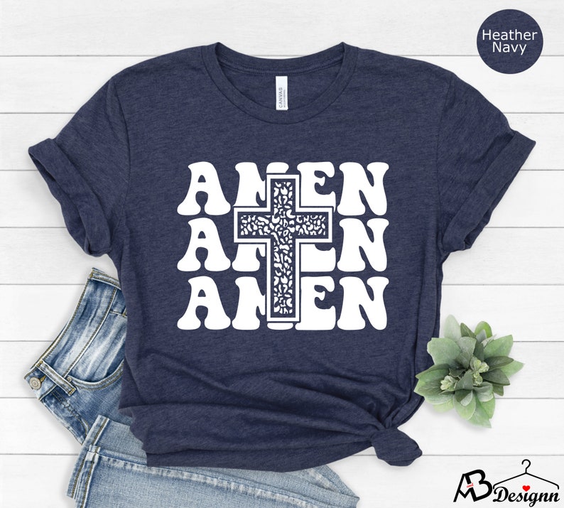 May include: A navy blue t-shirt with a white graphic of a cross and the word "AMEN" repeated three times. The cross is filled with a floral pattern.